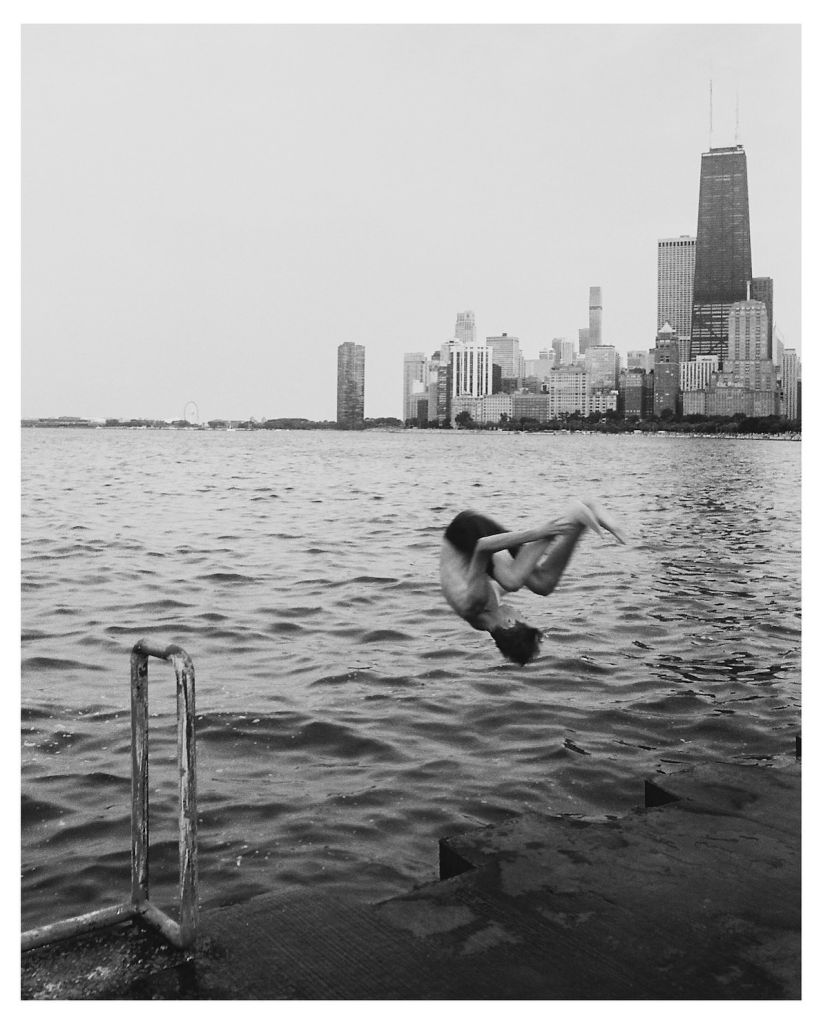 Personne sautant dans l'eau. En arrière-plan, des buildings