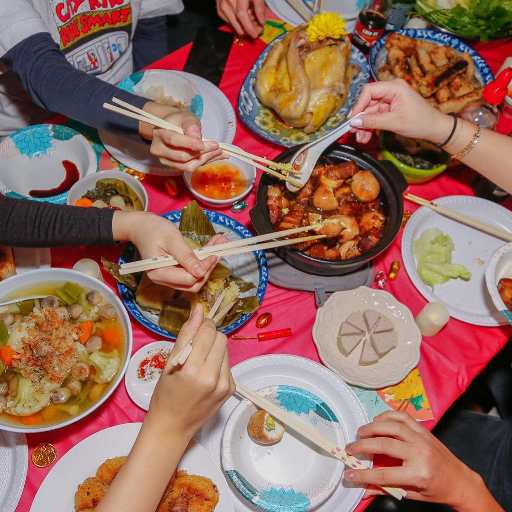 Festin vietnamien. Des mains tenant des baguettes se pressent sur les mets.