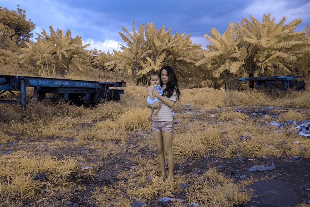 Une jeune femme tient son bébé dans les bras dans un paysage d'herbes.