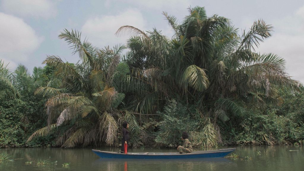 Deux femmes sur une pirogue qui vogue sur une rivière. Des palmiers en fond.