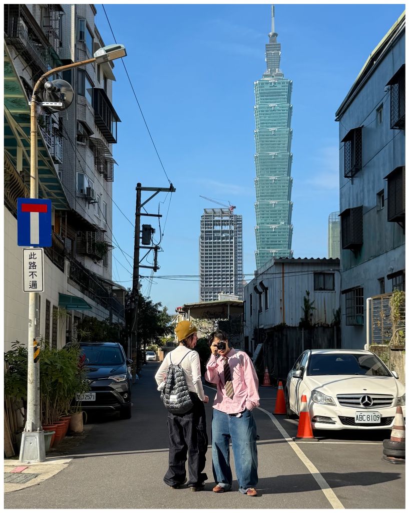 Deux personnes avec style posent dans une rue à Taipei, la Tour 101 en fond.