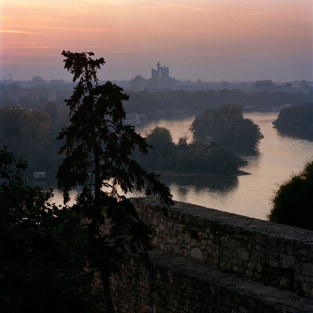 Paysage avec une ville au loin, un arbre et un fleuve au premier plan au coucher du soleil