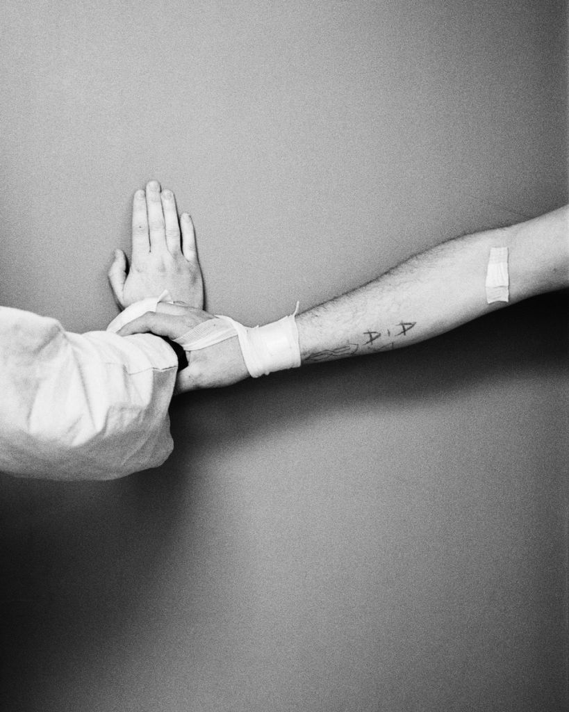 photo en noir et blanc, une main tient le poignet d'une autre personne dont la main est posée contre un mur