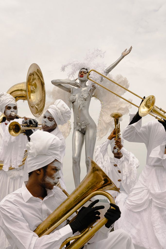 Une figure mi-femme mi-ange argentée entourée de musiciens en blanc