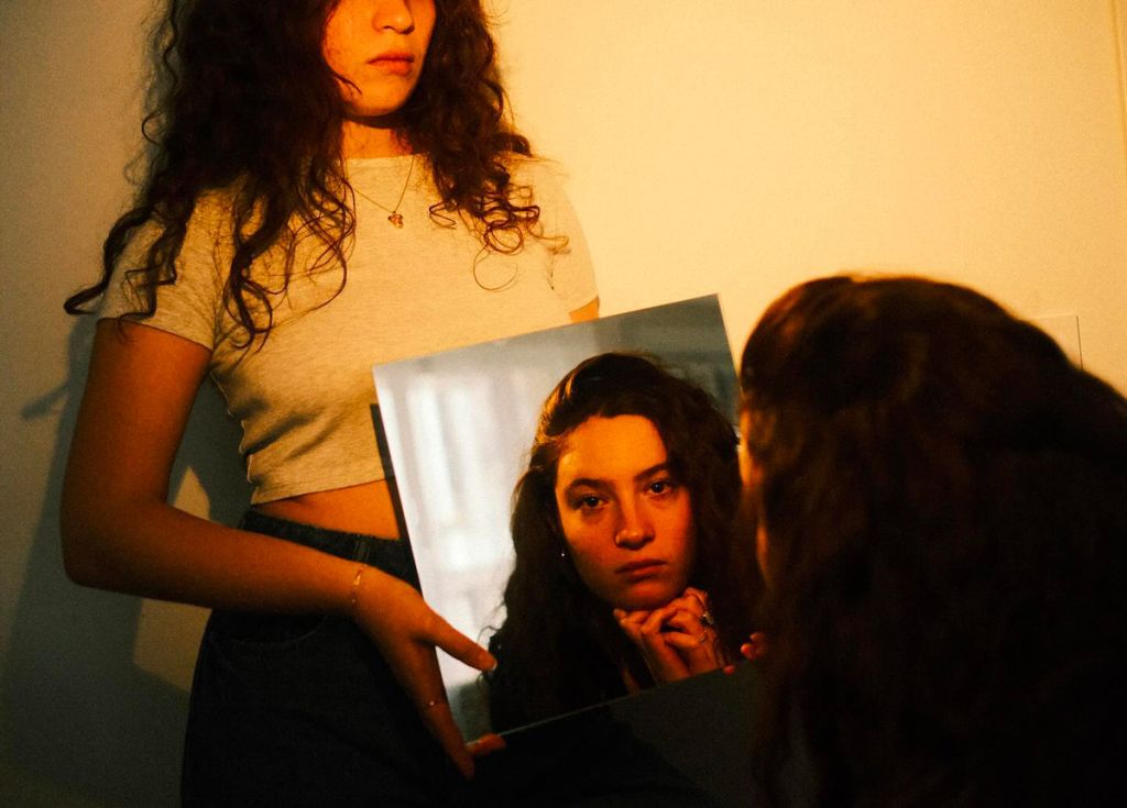 Une jeune femme se regarde dans un miroir, tenu par sa jumelle. 