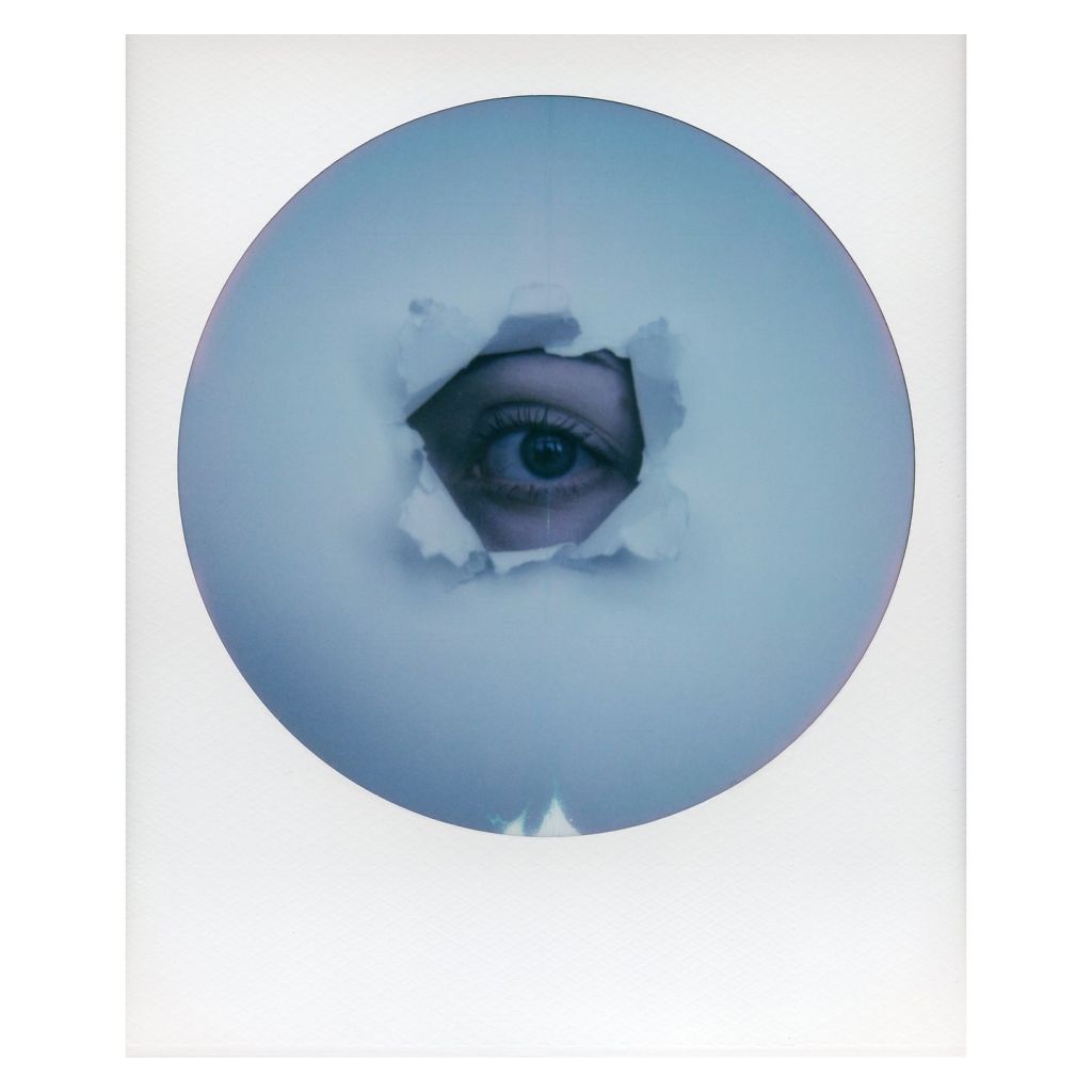 Polaroid d'un œil à travers un trou dans du papier