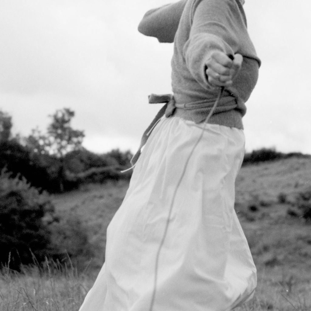 Le corps d'une femme en train de courir dans un paysage de nature, un fil (le déclencheur de l'appareil ?) à la main. 