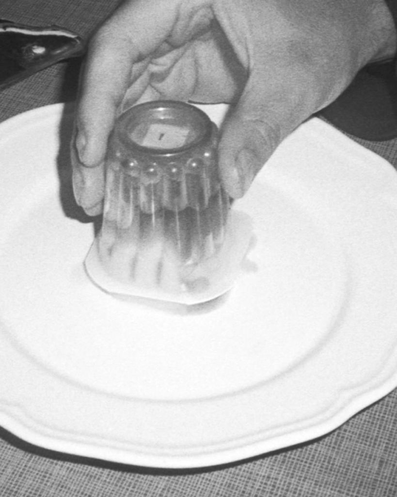 Une main tient un pot de yaourt à l'envers sur une assiette. 