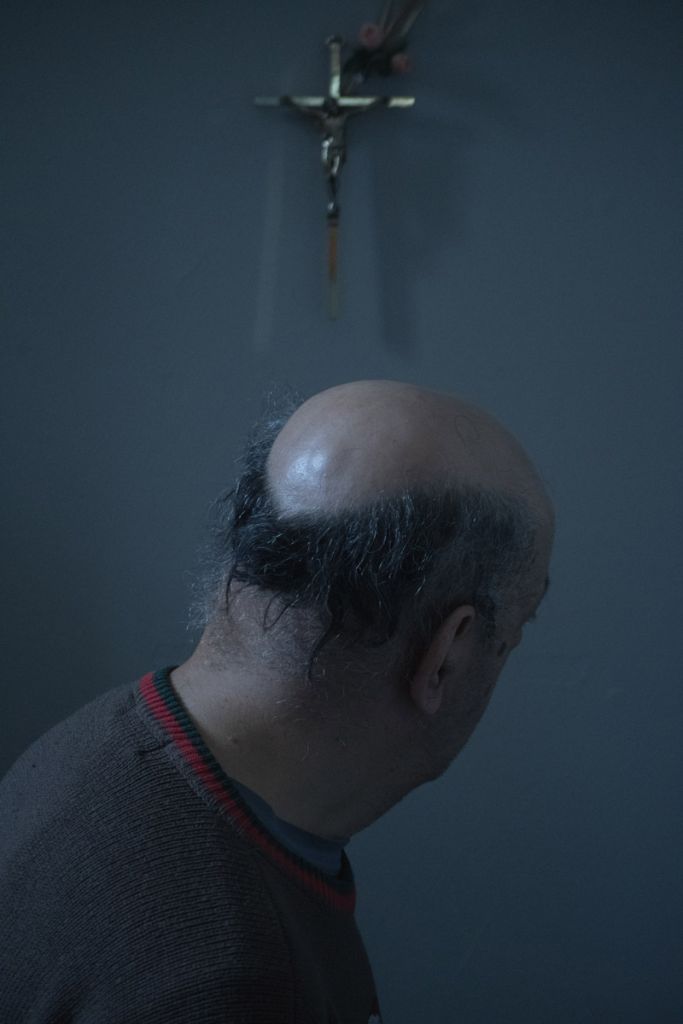 Portrait d'un homme âgé, le visage tourné vers le mur dans le fond, où est accrochée une croix.