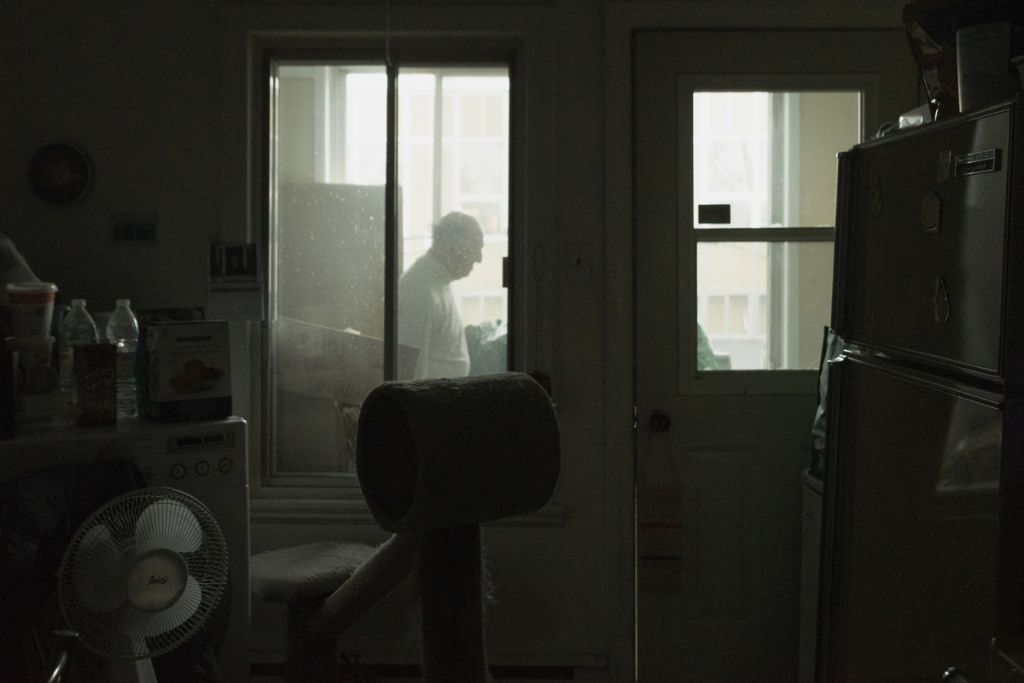On voit à travers une vitre dans un intérieur un homme marcher.
