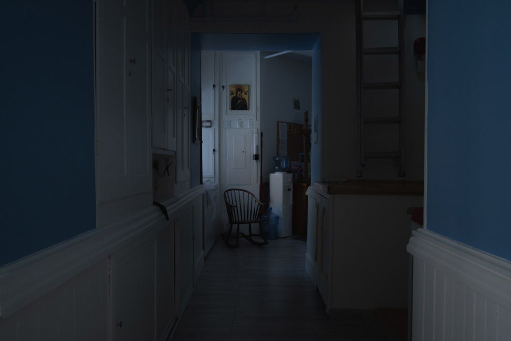 Intérieur d'un appartement, au bout du couleur se trouve une chaise vide et un tableau de la Vierge accroché au mur.