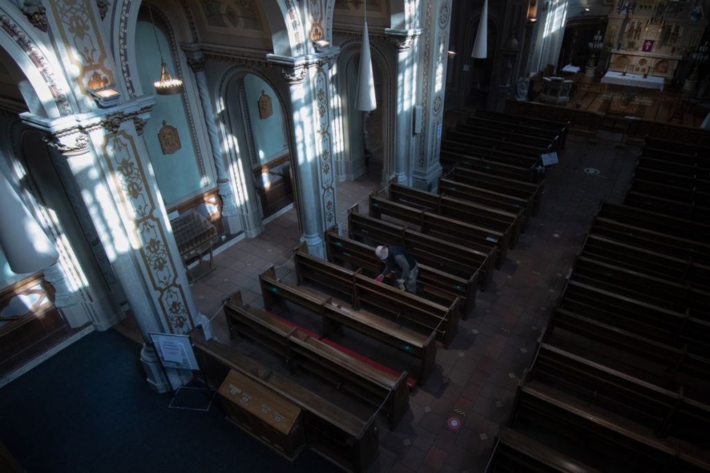Un homme vu en plongée nettoie les bancs d'une chapelle.