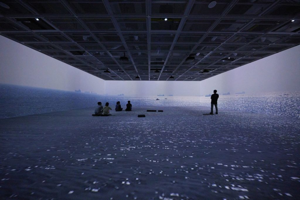 Des spectateurs dans une salle à 360° où l'on se retrouve en pleine mer, avec les bateaux au loin.