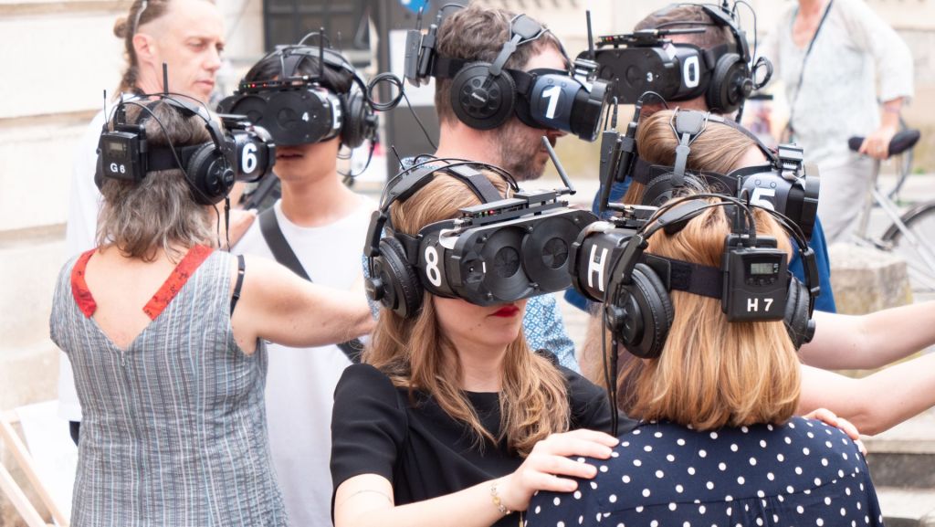 En extérieur, des spectateurs échangent et se touchent via un casque VR.