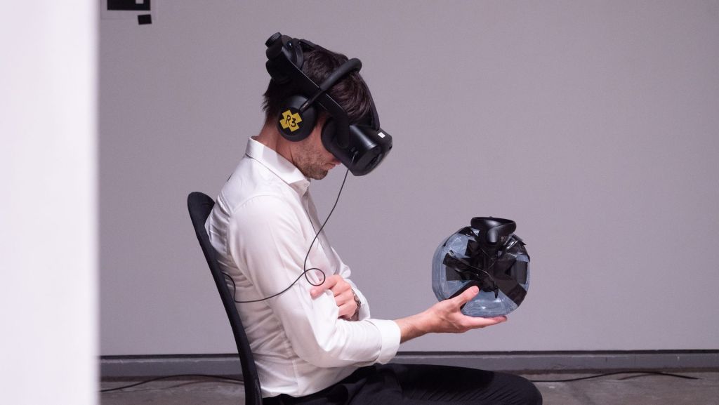 Un homme assis avec un casque VR sur la tête tient un objet entre les mains.