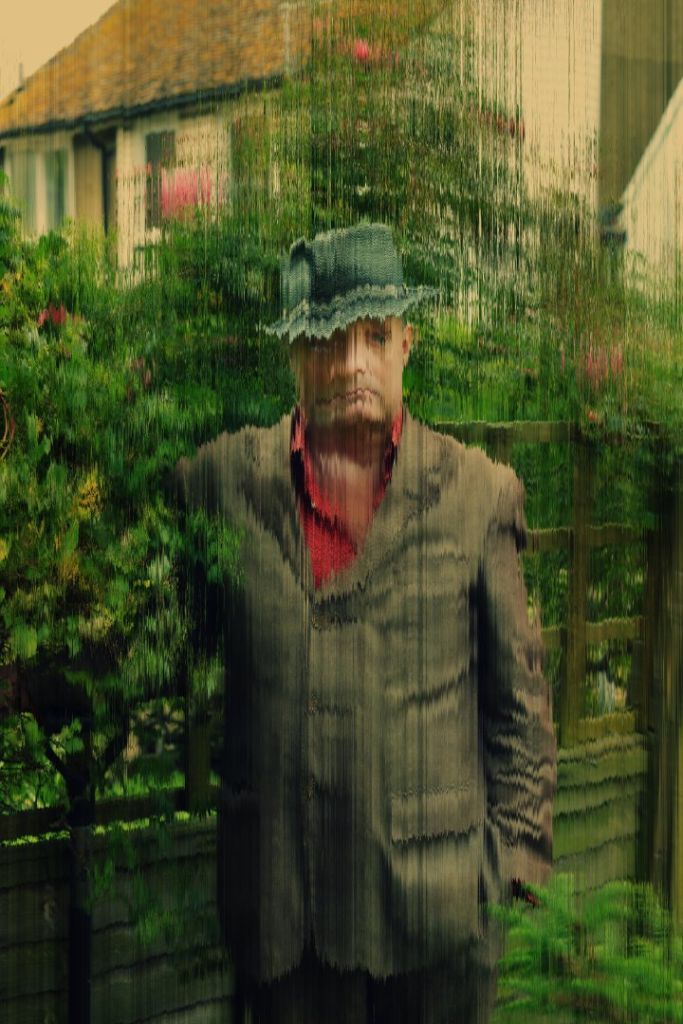 Un homme posant dans un jardin face à un objectif recouvert de gouttes de pluie.