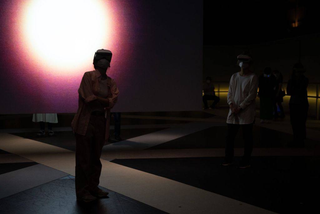 Deux spectatrices dans la pénombre d'une salle d'exposition, un casque VR sur la tête.