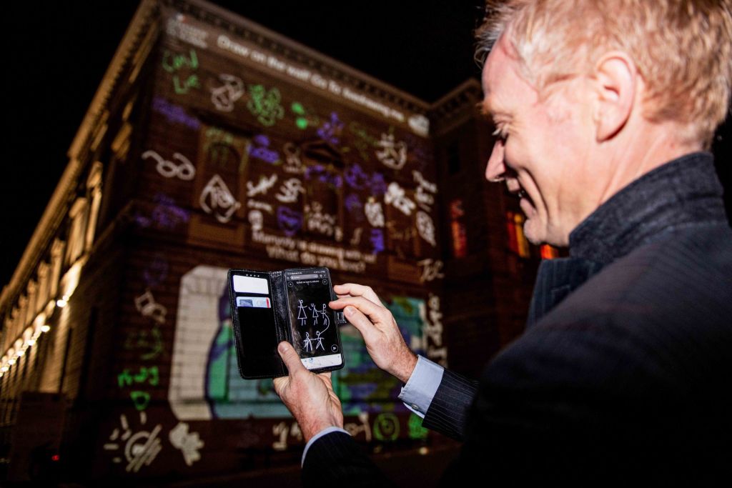 Un homme dessinant sur son portable des personnages projetés illico en vidéo-mapping sur la façade en face de lui.