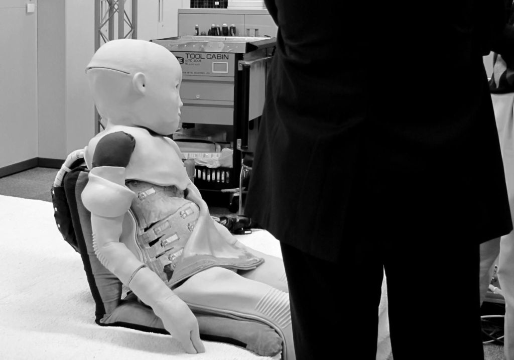 Une photo en noir et blanc montre un homme en costume, de dos, aux côtés d'un robots d'apparence humaine.