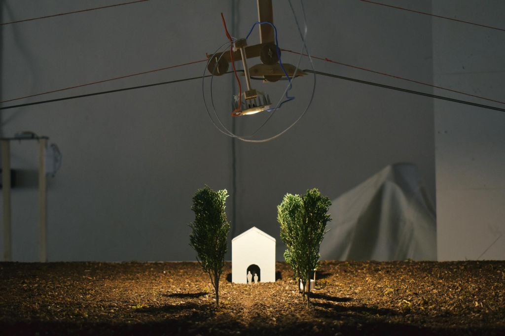 Version miniaturisée d'une maison blanche entourée par deux arbres et éclairée par des lumières artificielles.