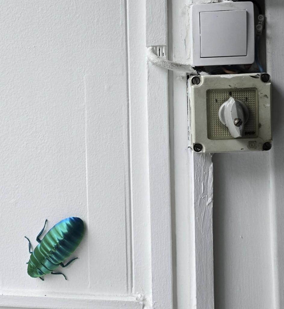 Un insecte vert en impression 3D posée sur une porte blanche.