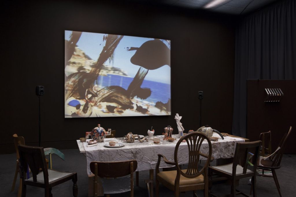 Installation où une table à manger est installé dans une pièce face à un écran plat diffusant un film.