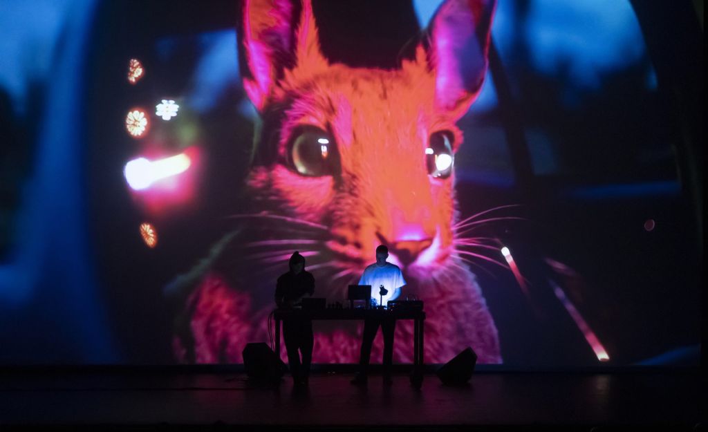 Deux artistes mixent sur scène, dans le noir, pendant qu'un écran géant diffuse les images d'un lapin rouge.