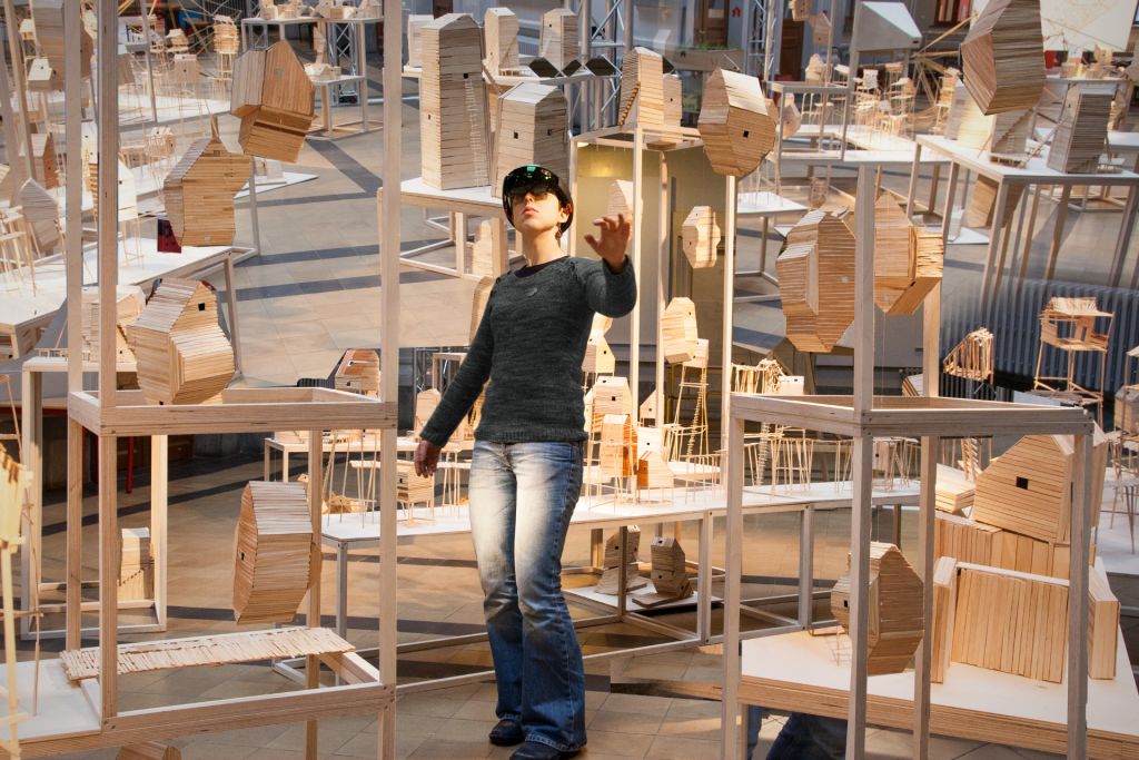 Une femme avec un casque VR au milieu d'installation de maisons en bois.