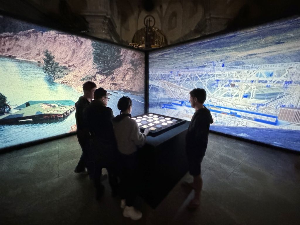 Quatre spectateurs face à une table de jeu dans une pièce entourée d'écrans immersifs.
