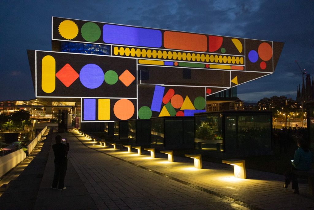 La nuit, un bâtiment sur les hauteurs de Barcelone est éclairé par un mapping de formes circulaires et colorées.