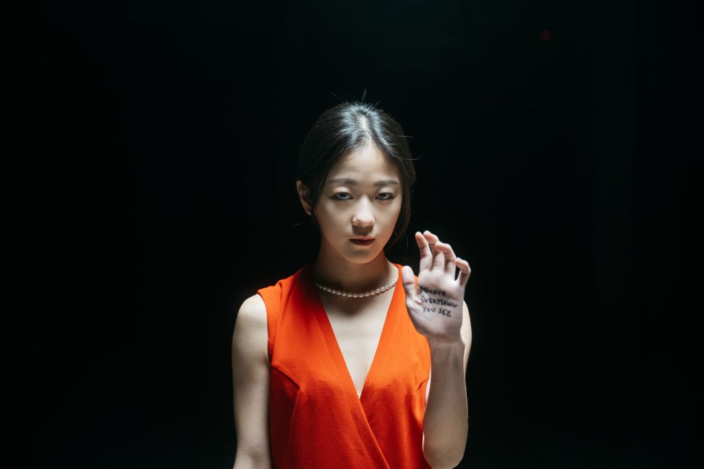 Gros plan d'une jeune femme asiatique en robe orange, dans le noir.